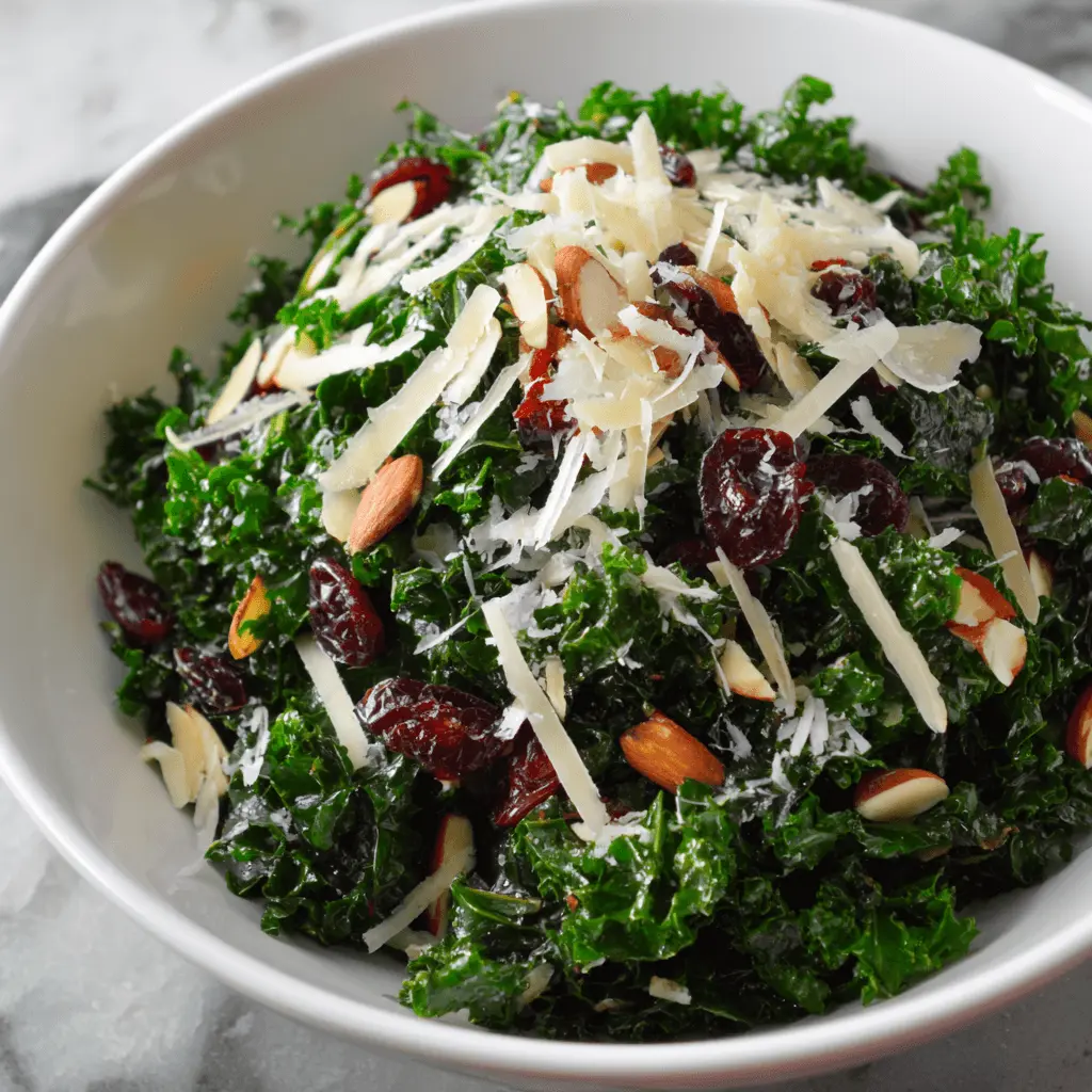 Vibrant kale salad with dried cranberries, shaved Parmesan, and blanched almonds in a white ceramic bowl, ready to be enjoyed.